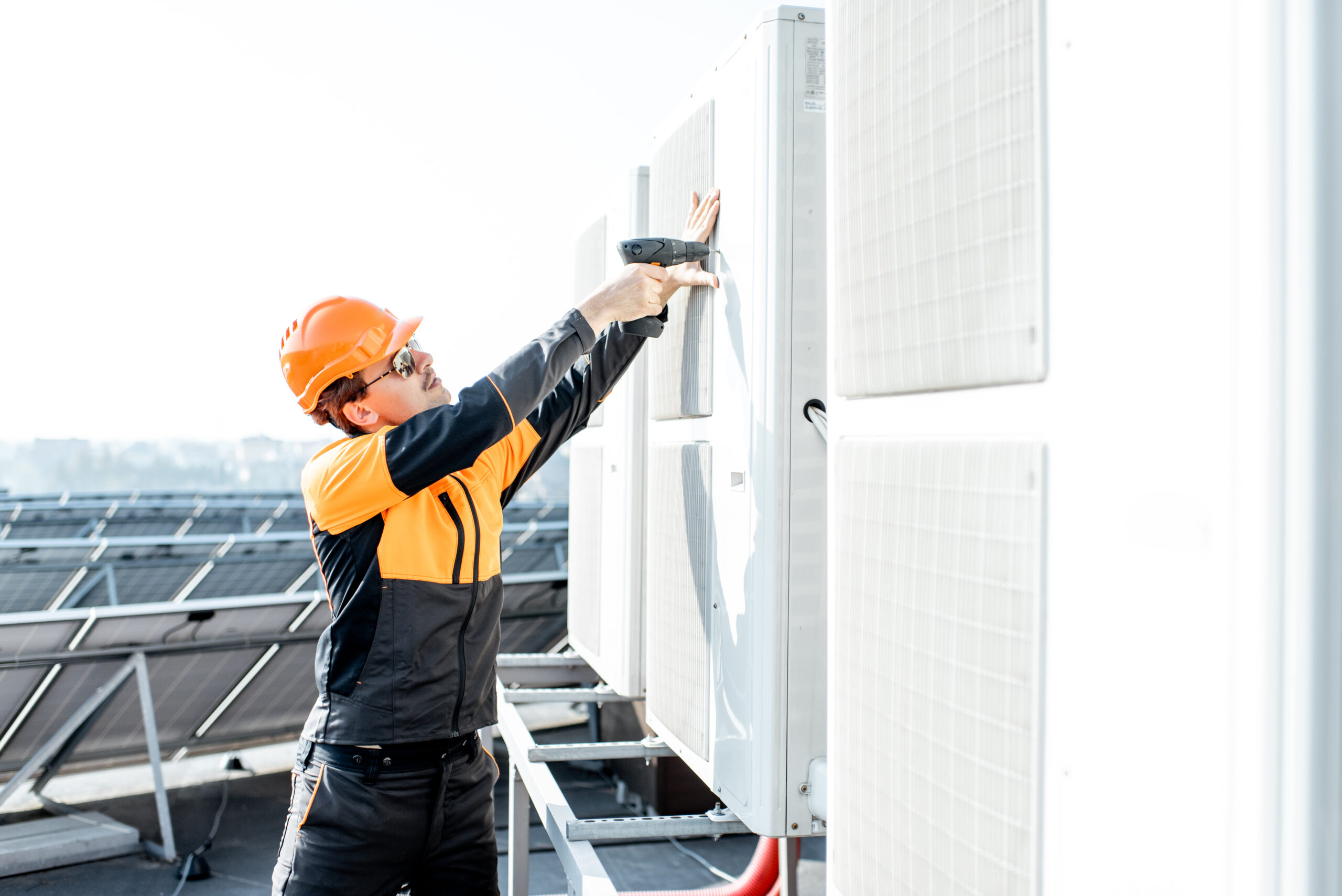 Professional workman in protective clothing installing or reparing outdoor unit of the air conditioner or heat pump on the rooftop
